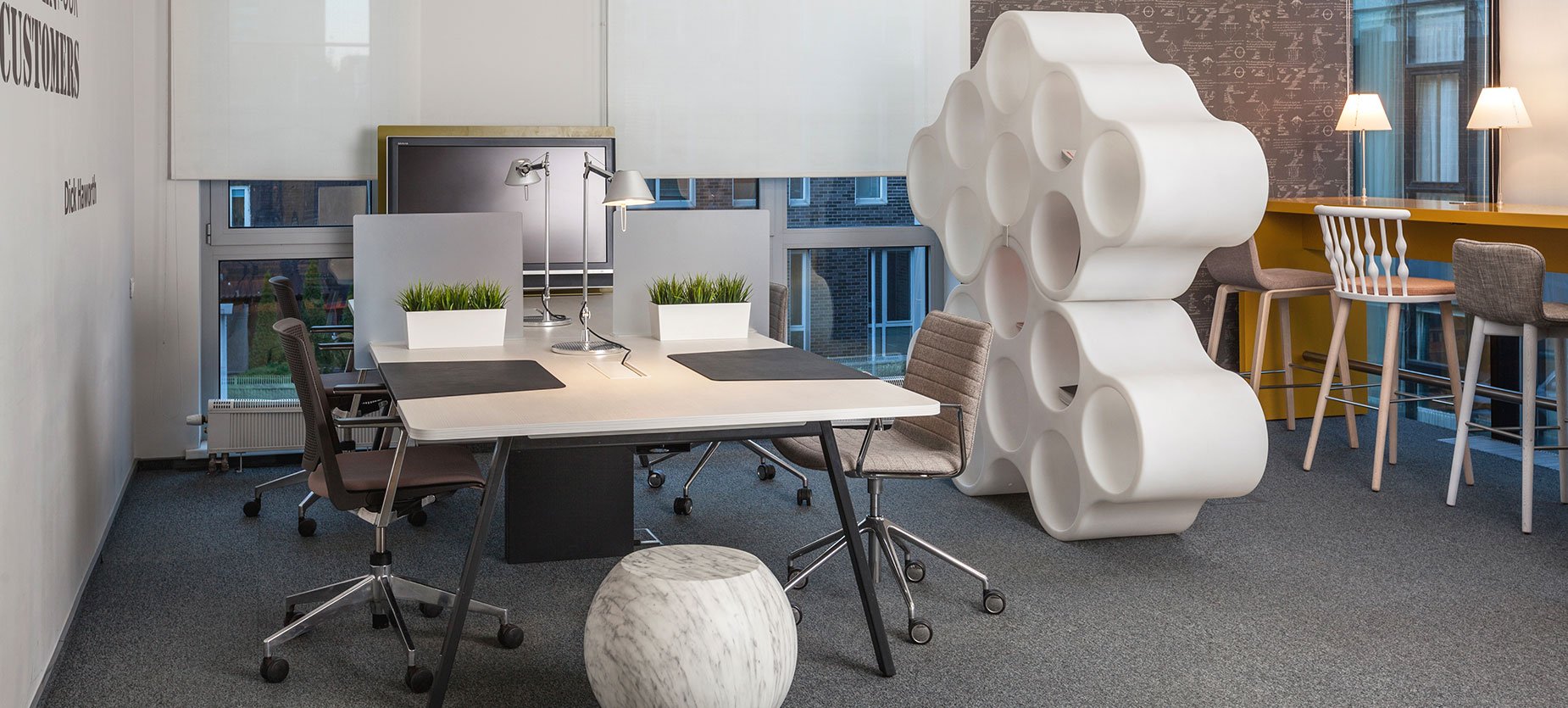 This hot-desking space features a four-person bench with movable screens and a display. Cloud storage serves as a space divider between desks and the bar table, which accommodates for sit/stand work.