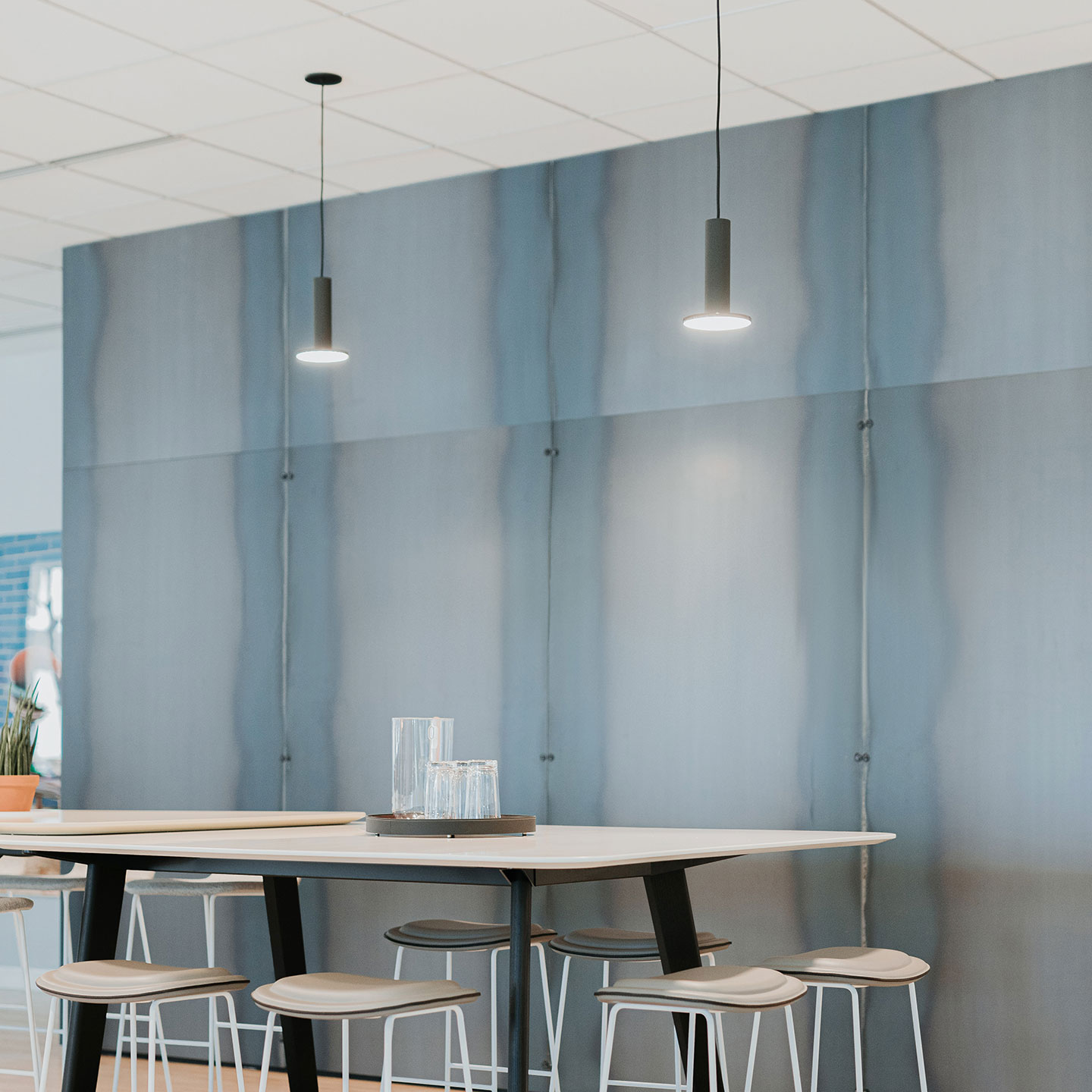 Haworth Cielo Lighting in grey hanging from wall with white table and white chairs in open office setting with blue wall dividing 