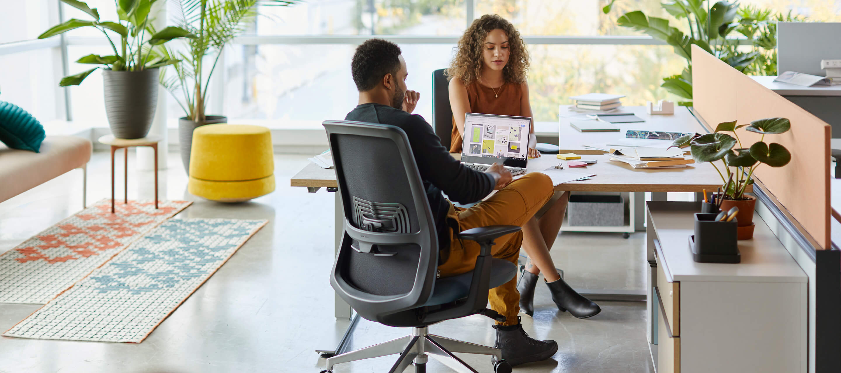 Two employees collaborating over a desk in a sunny office space