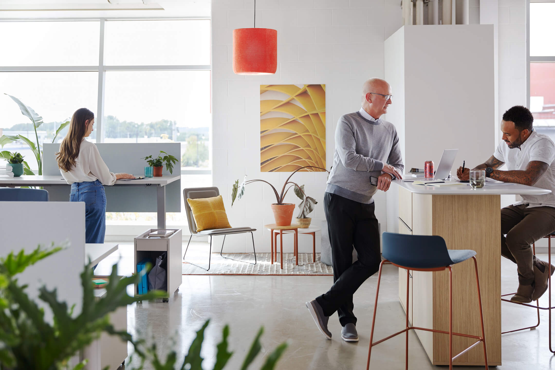 Open office space showing sit to stand desks and a table that is being used for collaborative work