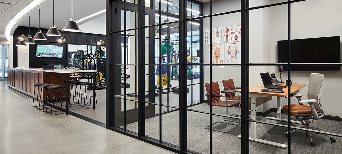 Attracting the best talent and a focus on health and well-being are two drivers behind the space design. This impressive training area highlights advanced weight-training equipment separated by a sleek black-accented glass wall. The training manager has visibility from his office behind the glass. A Planes® height-adjustable table, Exchange™ guest chairs, and a Zody® task chair provide functionality and comfort for athletes and their trainers in a small collaborative area used for relaxing, hydrating, or interacting. X Series® storage provides a solution for a variety of storage needs and requirements.