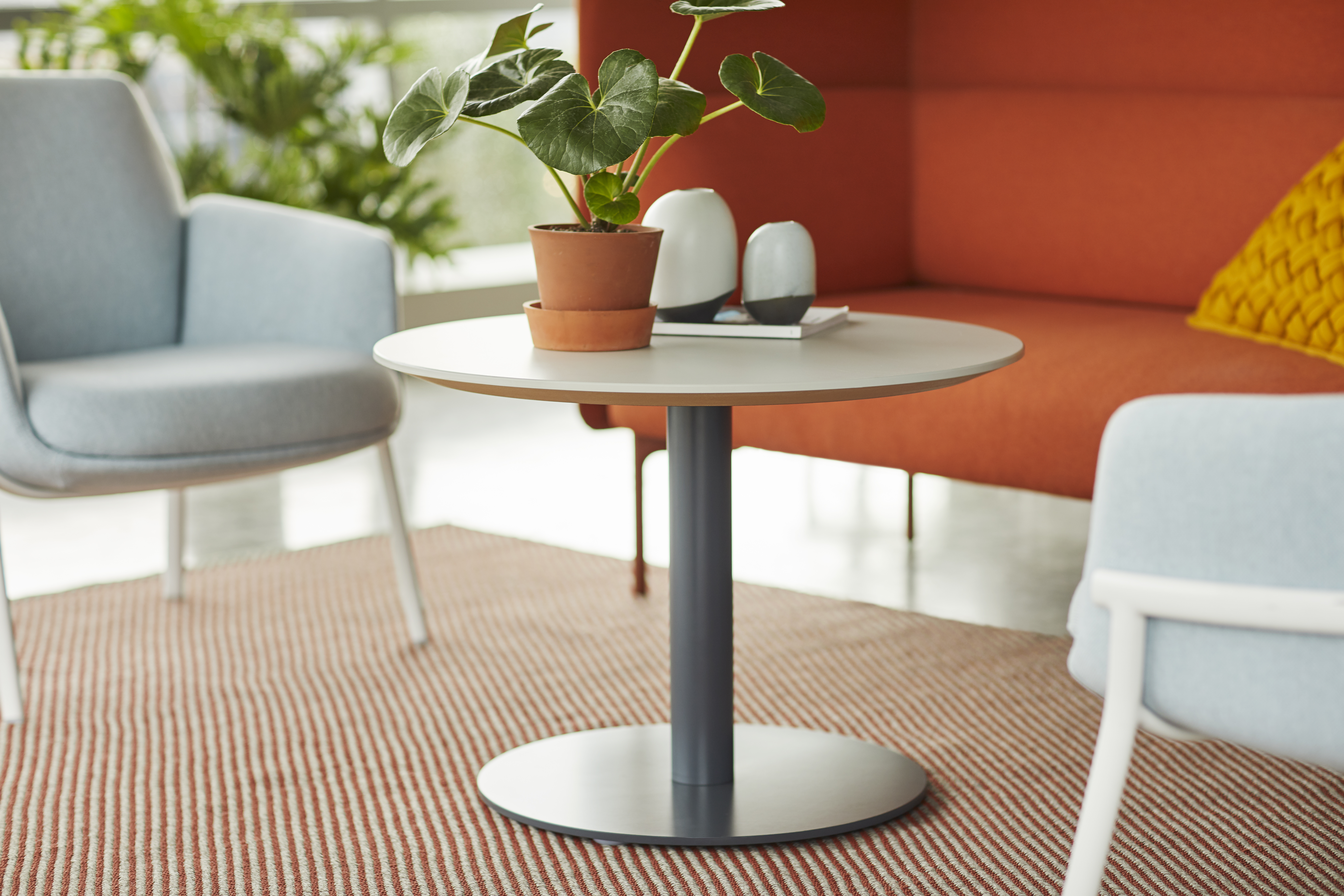 Haworth Planes Collaborative Table with white circular top in a office area with a cabana lounge chair and diagonales rug