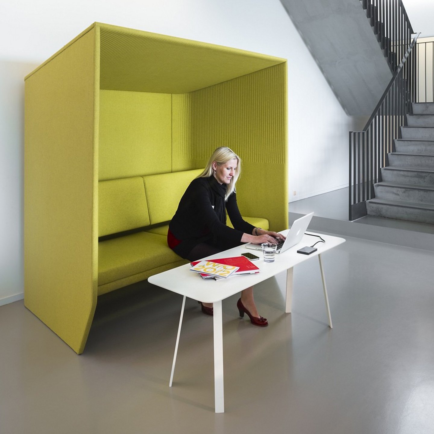 Haworth BuzziHub Booth in lime green color with employee working inside it and at white table next to staircase