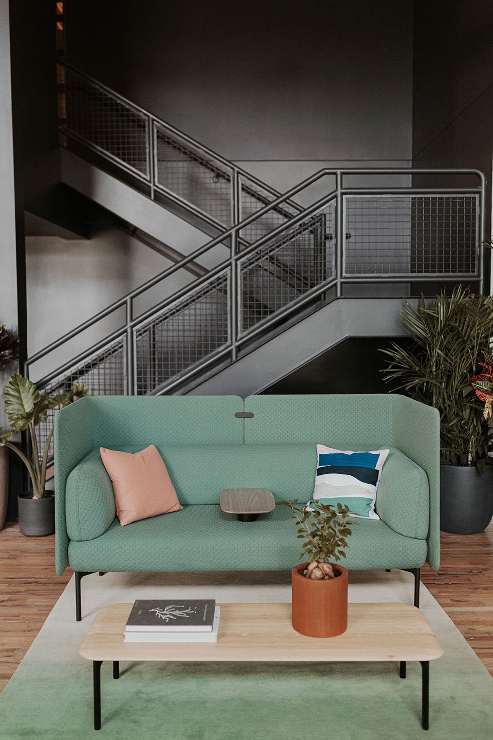 Haworth Cabana Lounge in green color with green rug underneath and black staircase with wood table 