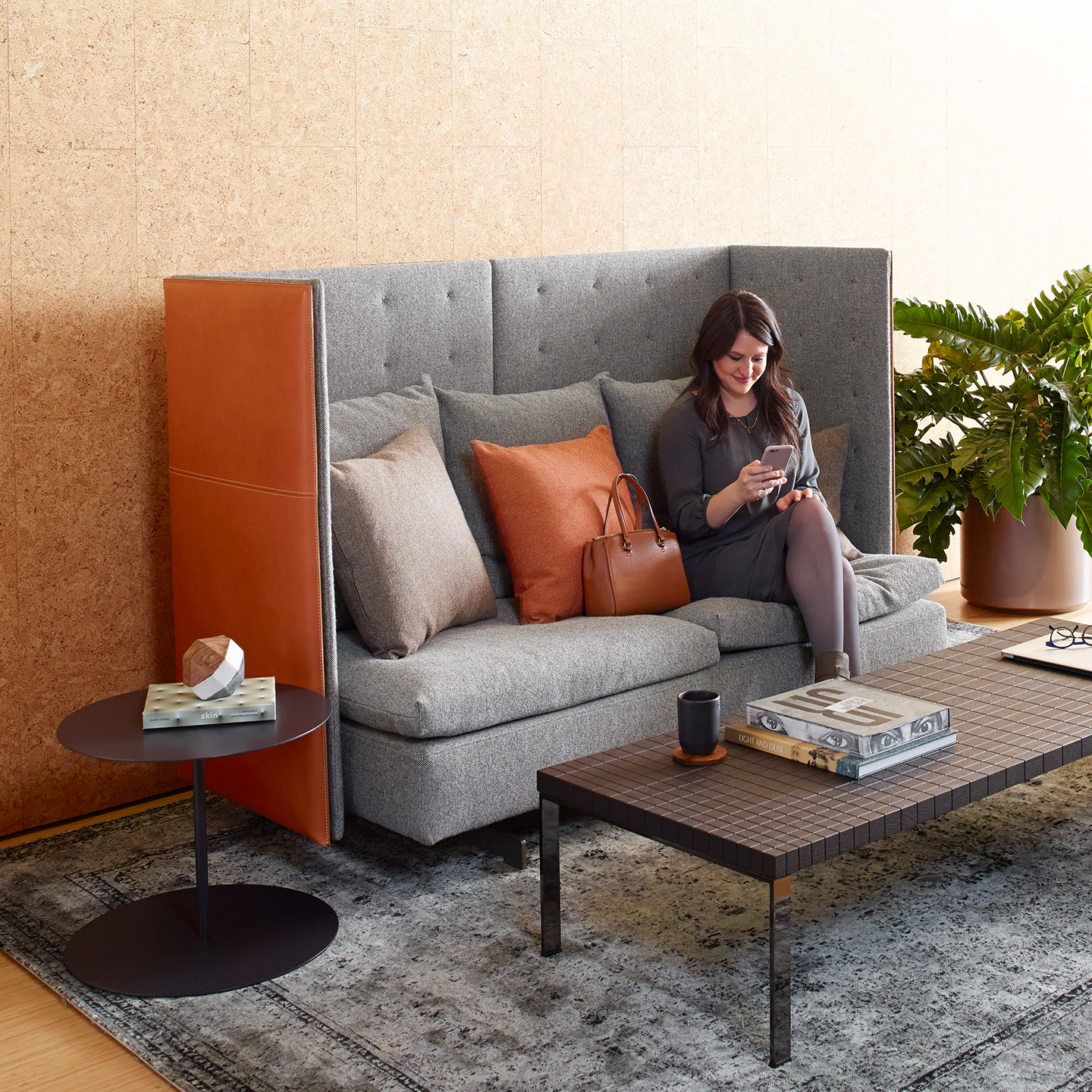 Haworth GranTorino HB Booth in grey color and orange back with employee sitting in it with wood coffee table in front of it 