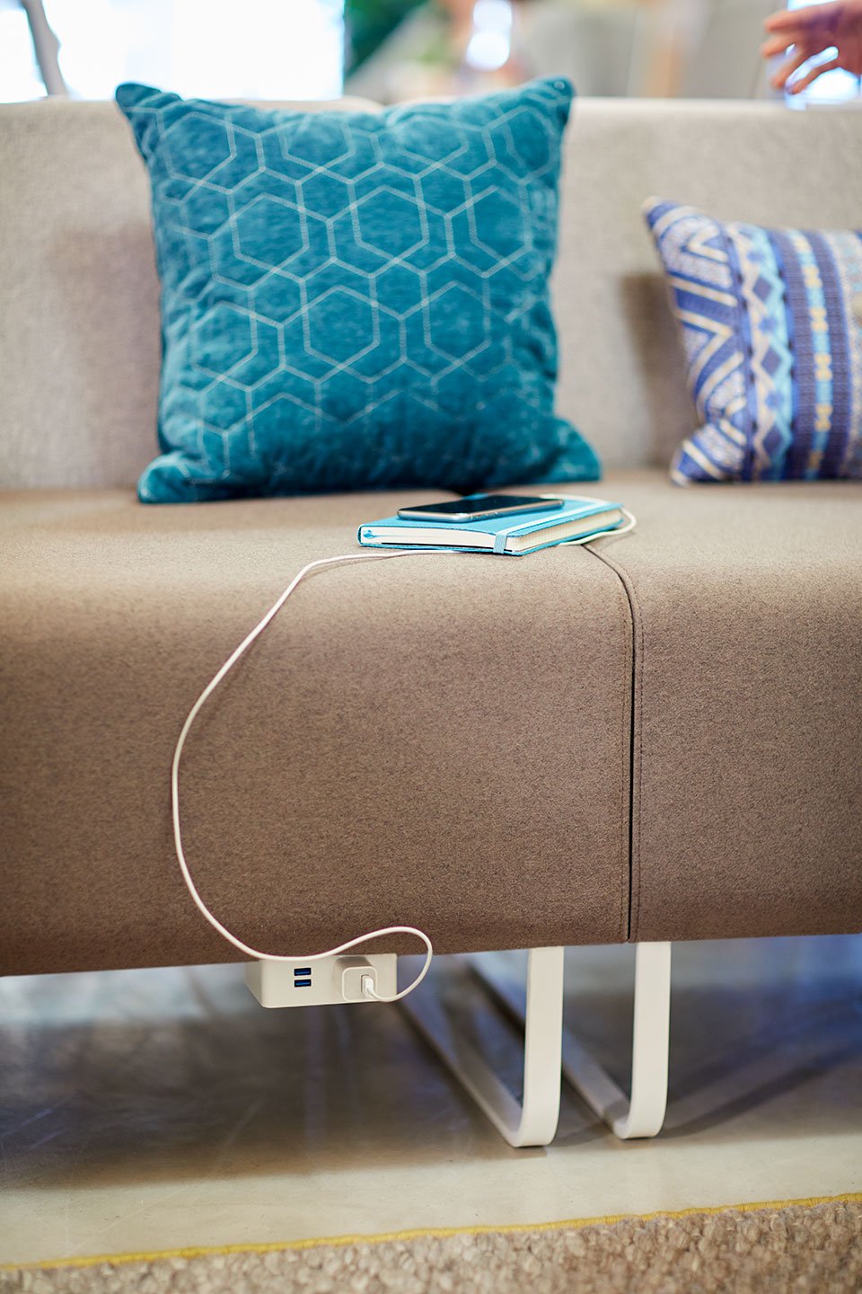 Haworth Riverbend and Pebble Booth in grey color with phone plugged into port with throw pillows on couch