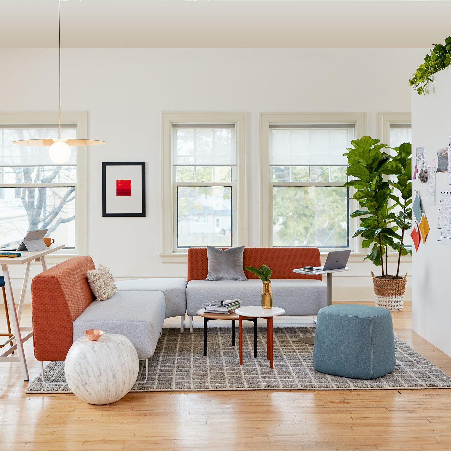 Haworth Riverbend and Pebble Booth in grey and red color in office space with white center table and ottomans around it