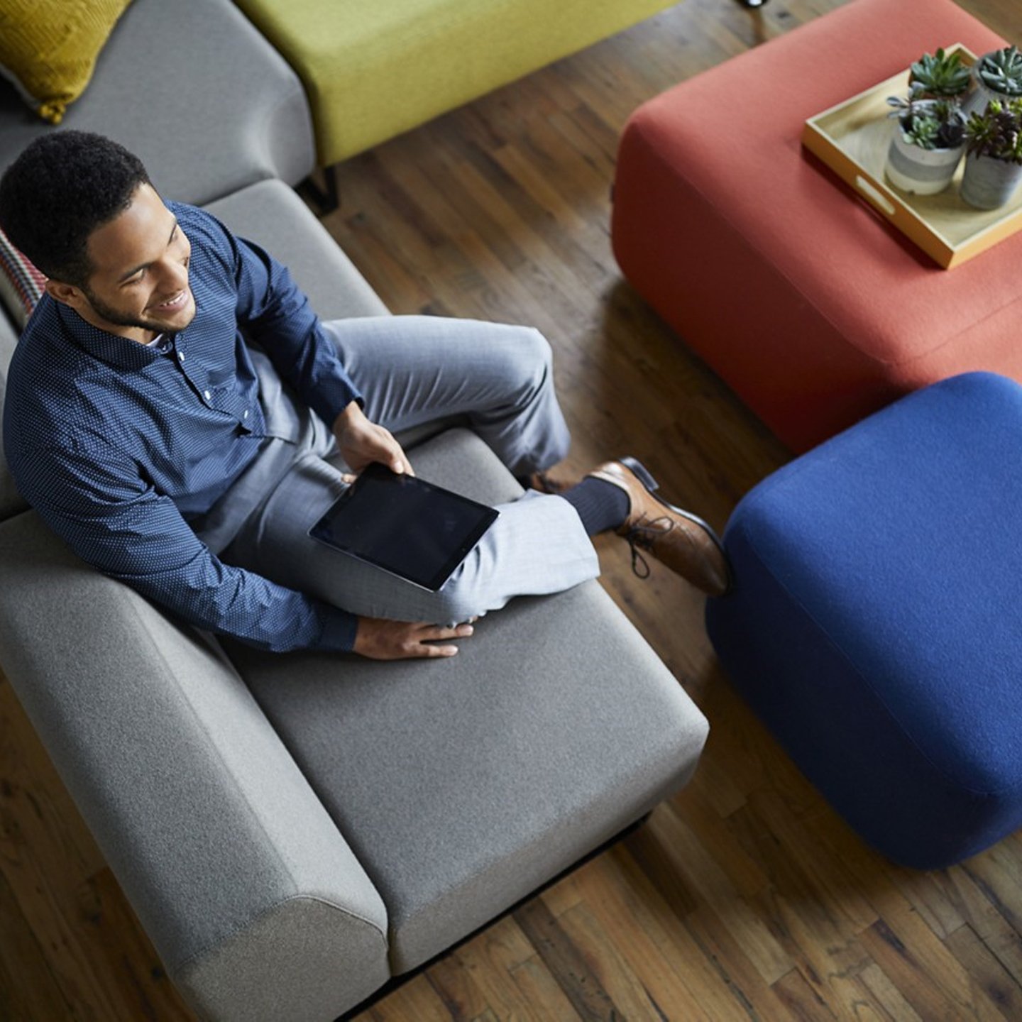 Haworth Riverbend And Pebble Booth in grey color with employee sitting next to blue and red ottoman