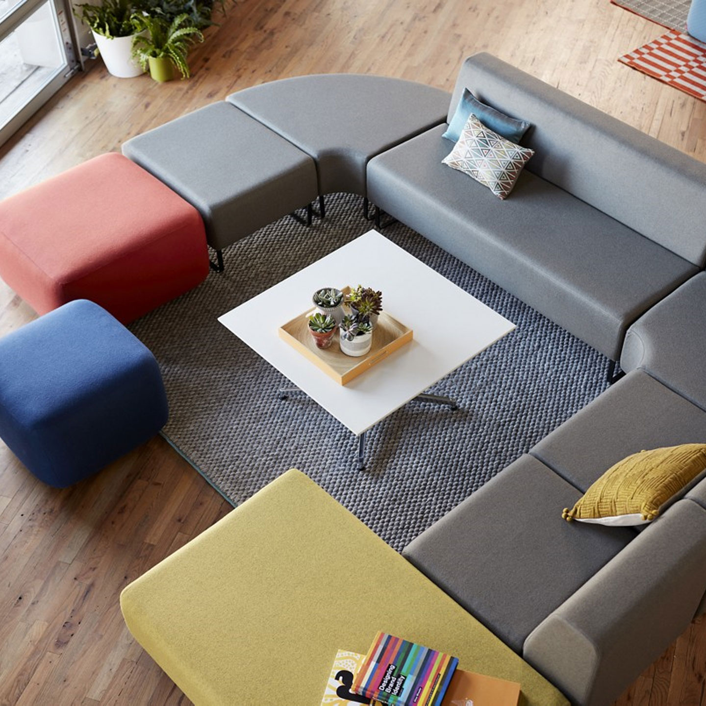 Haworth Riverbend and Pebble Booth in grey color with red blue and yellow ottmans near it with white center table in open space