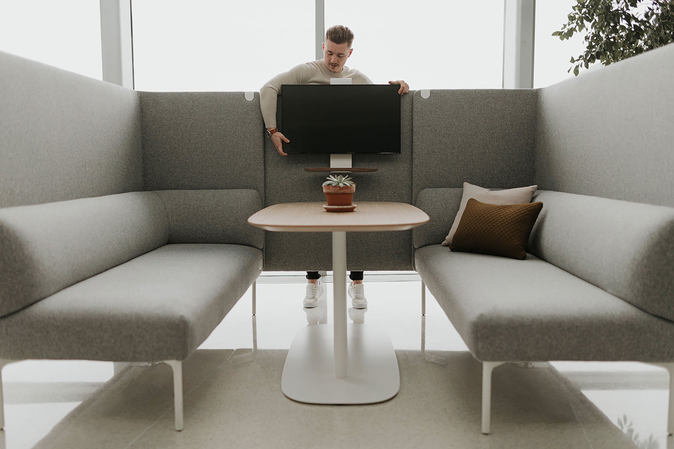 Haworth Cabana lounge connector screen being setup with a monitor screen by a coworker in an open office space