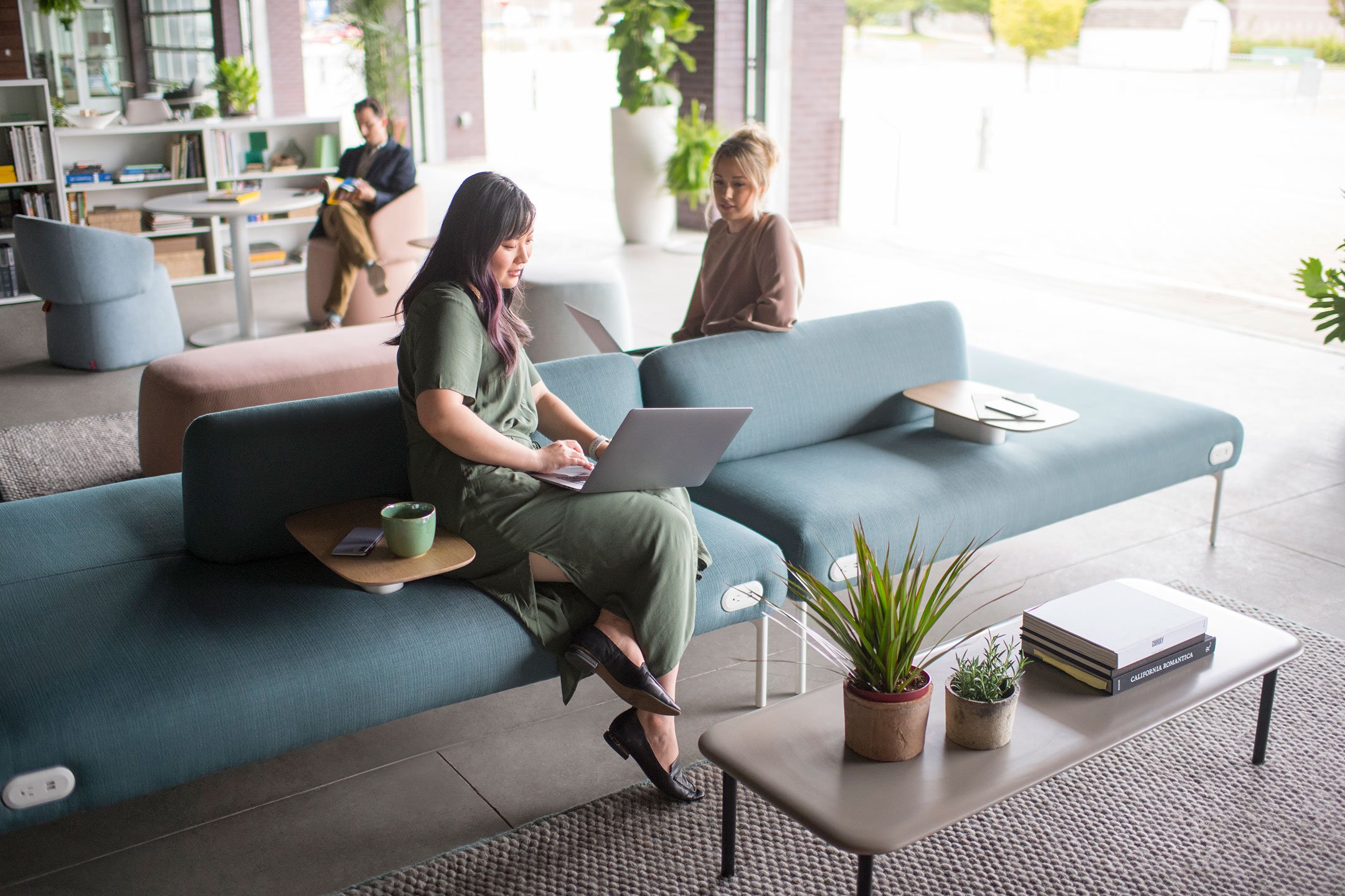 A couple of coworkers having a casual meeting on a green Haworth Cabana island lounge in a open office space