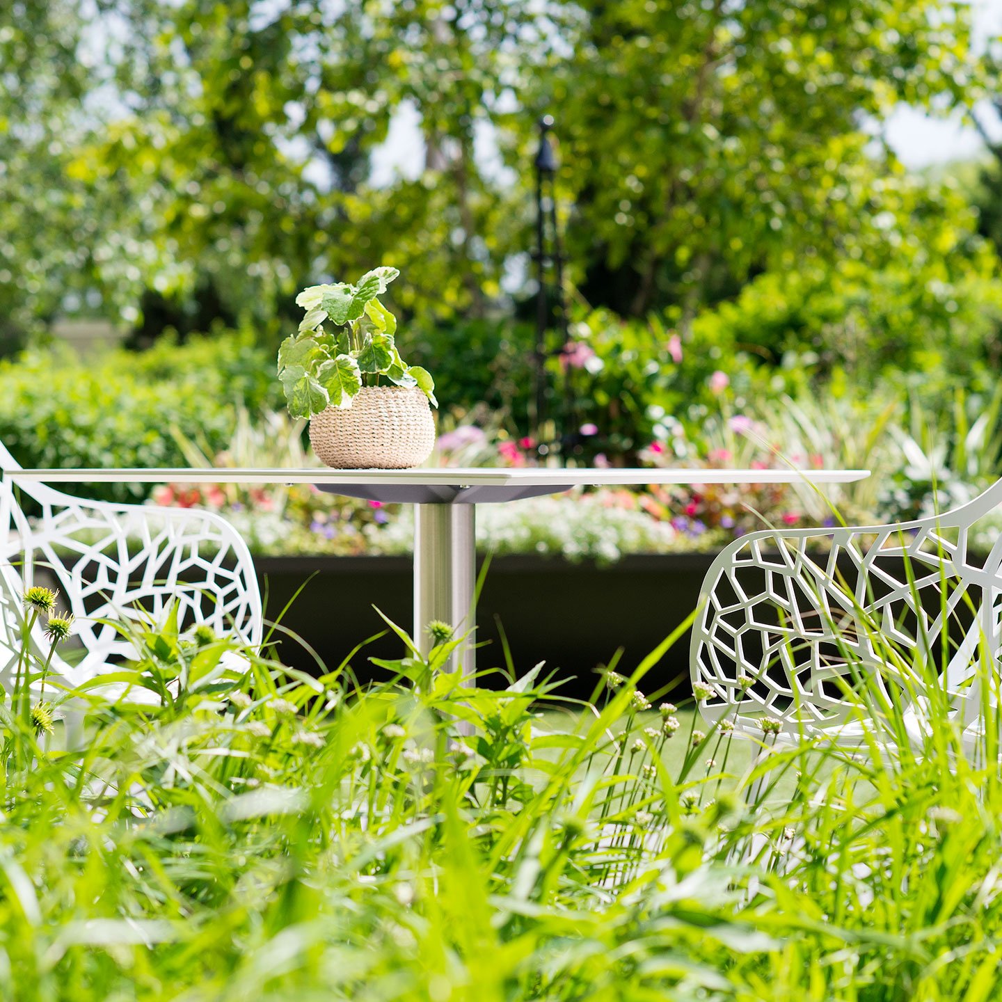 Haworth Janus Cafe Table with circular top in an outdoor seating area with flowers in the back 