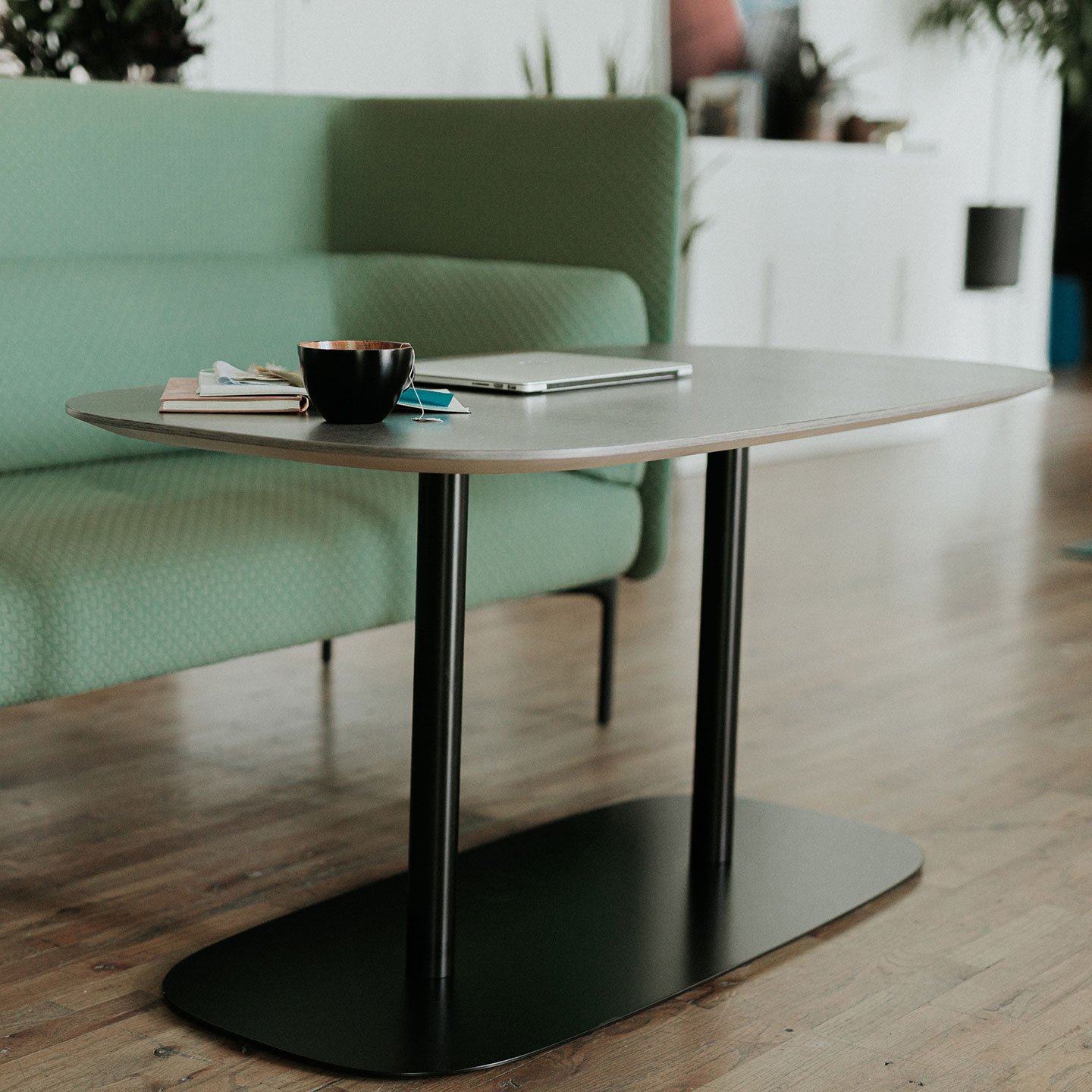 Haworth Pip Collaborative table in white by a green couch with a laptop and coffee on top of it