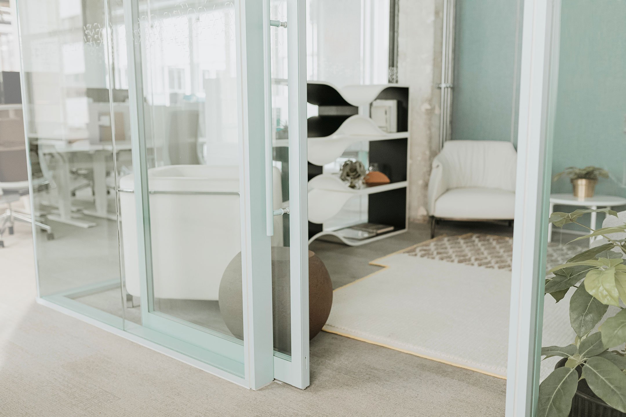 Haworth Enclose Frameless Glass 2 Wall in private lounge area in office with teal walls and white chairs