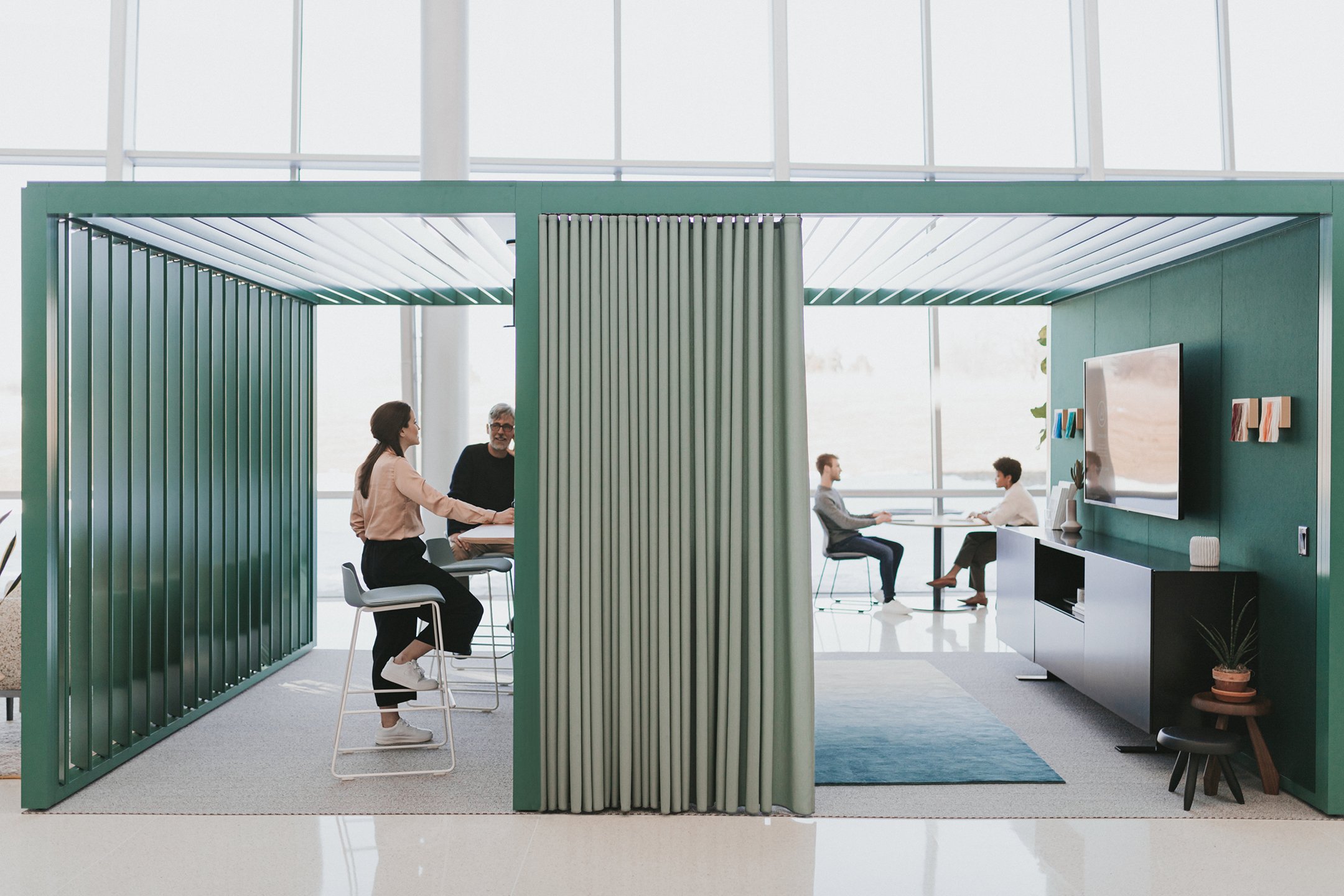 Haworth Pergola Workspace in green trim with storage in black and TV with employees working at high table in open office space