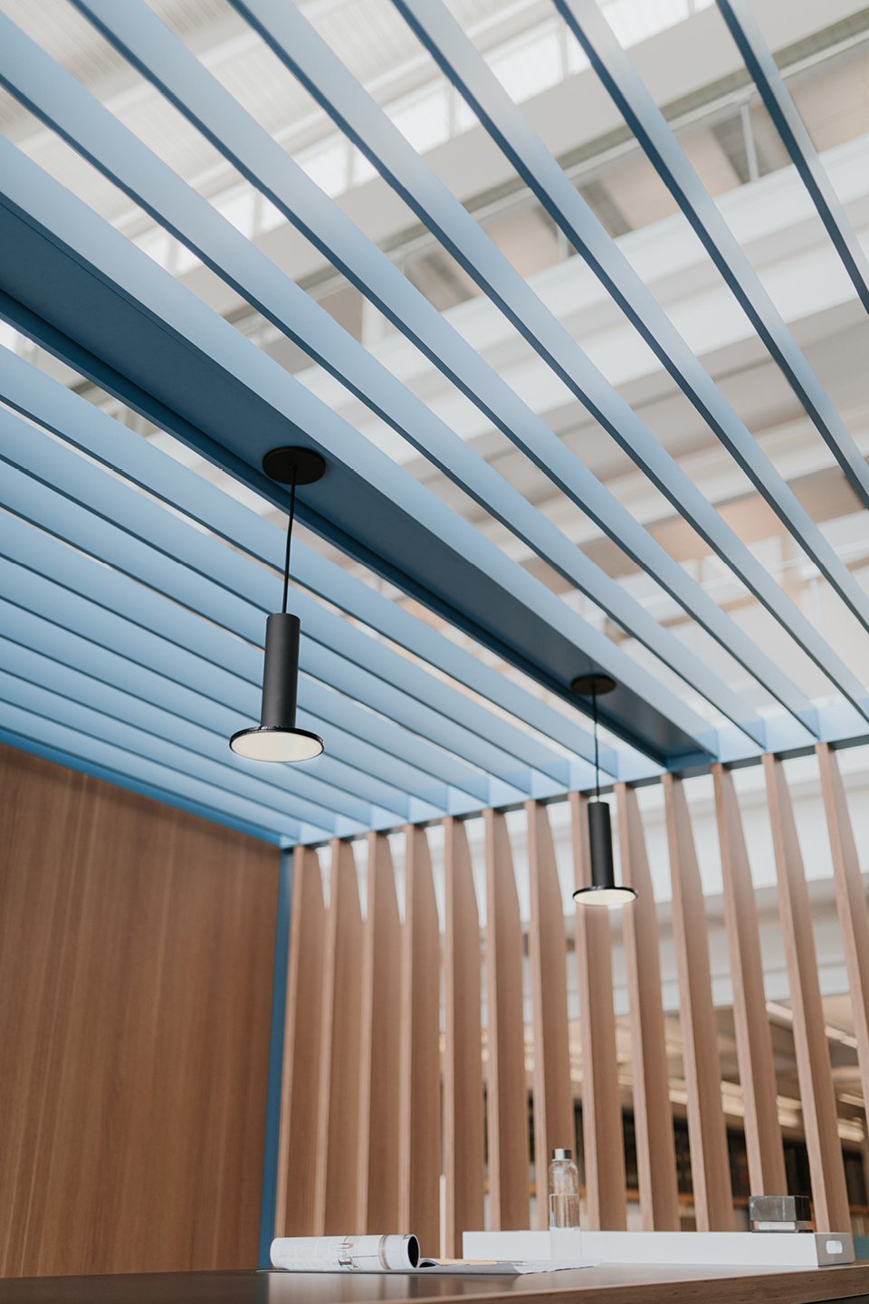 Haworth Pergola Workspace with veneer slits and blue beams on top with overhead lights hanging down over black table in office space