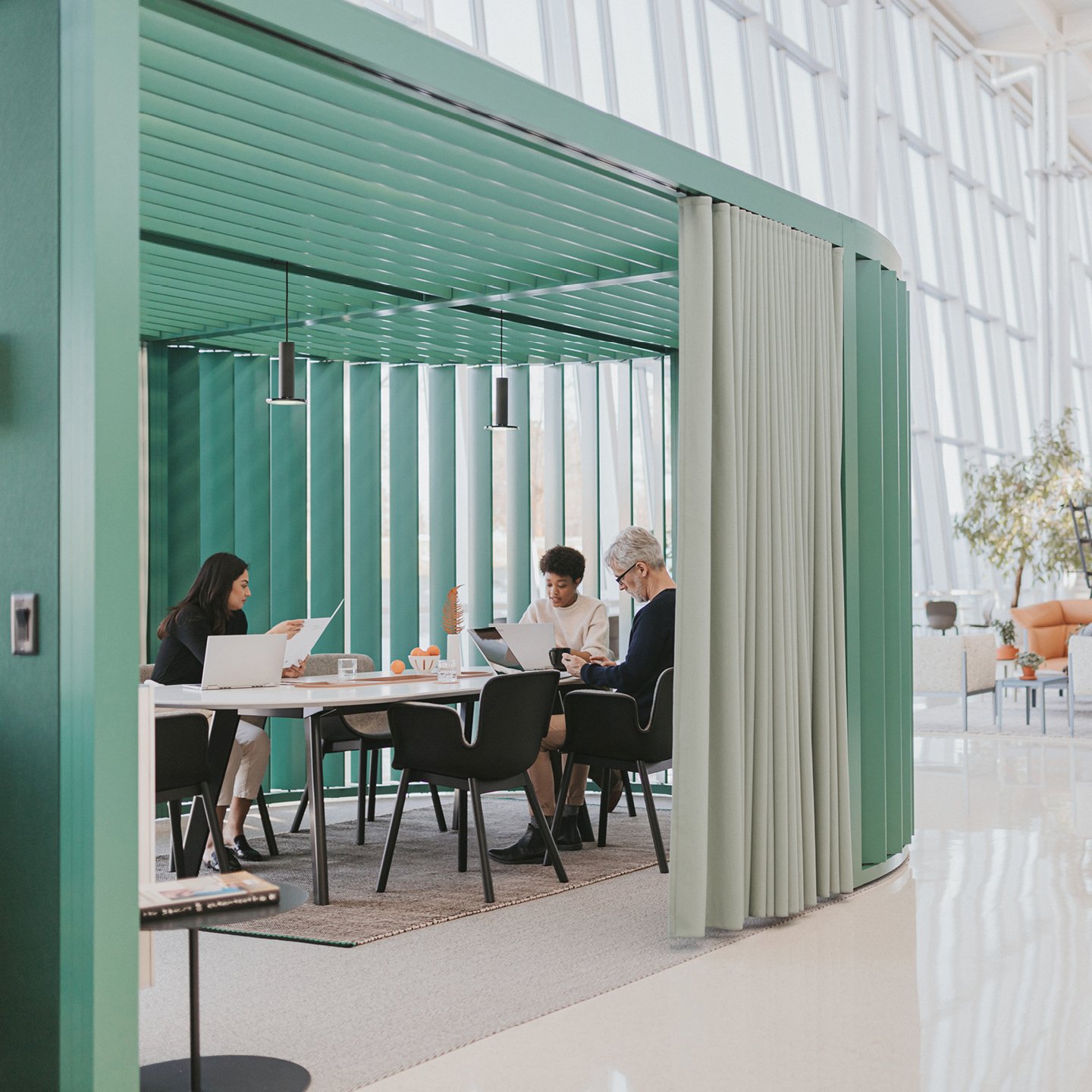 Haworth Pergola Workspace in green trim with green curtain with white table and black chairs and emloyees working on the table