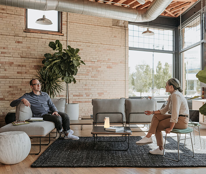 Haworth Bringing Employees Back to the workplace Spark employees sitting in open office area with grey couch wooden coffee table and small chairs